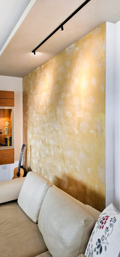 Seitliche Aufnahme einer goldenen Wand in einem Wohnzimmer mit einem Muster, welches durch einer Spachteltechnik vom Team Malermeister Bernhard Mrezar ausgeführt wurde
