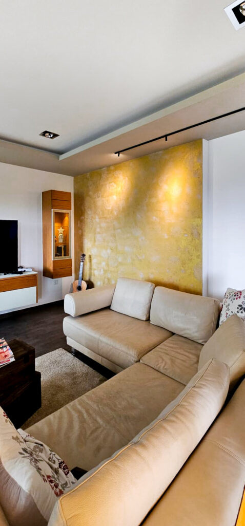 Aufnahme von einem Wohnzimmer mit einer goldenen Wand, in der Muster zusehen sind. Spezielle Spachteltechnik